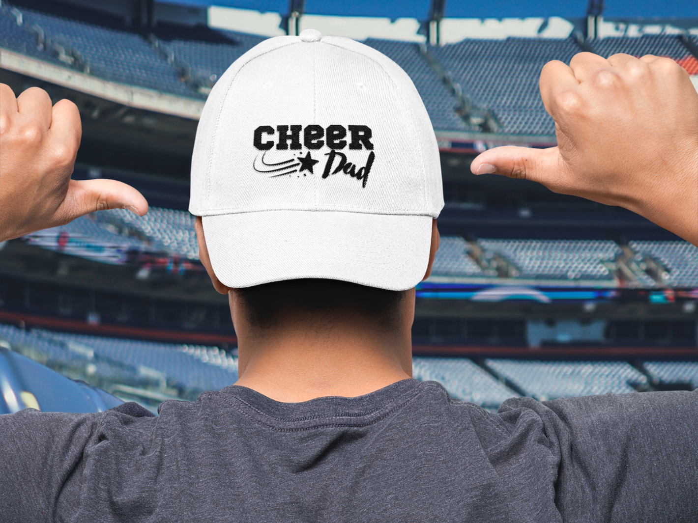 Cheerleading Dad pointing to his baseball cap with his thumbs in a football stadium